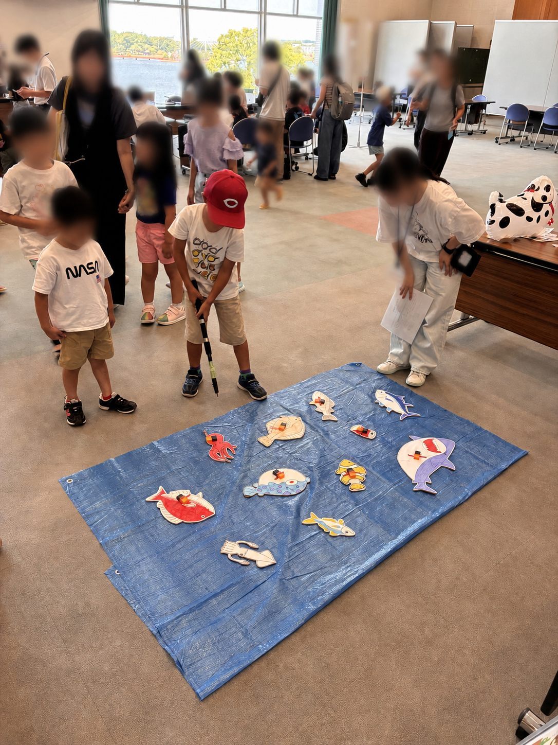 魚の模型を並べたシートで、子どもが釣りざおを使って魚釣りゲームを体験している様子